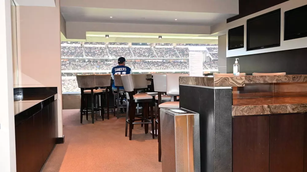 Spacious suite interior with additional seating at a hightop table in front of the 3 TV monitors.